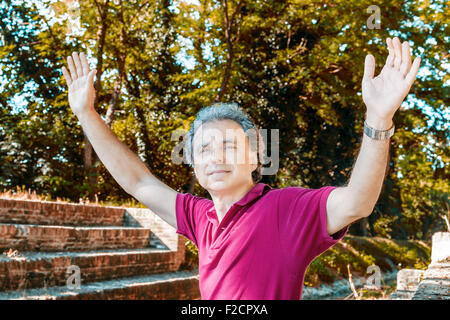 Beau et charismatique Caucasian sportsman de quarante avec cheveux gris polo porter du rouge foncé et un pantalon de lin est raising arms, assis sur l'ancienne cité médiévale de mesures du Canal de l'usine dans l'Émilie-Romagne en Italie Banque D'Images