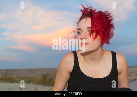 Une jolie jeune femme posant avec sérieux et réfléchis, expressions idiotes à l'extérieur contre un ciel bleu. Banque D'Images