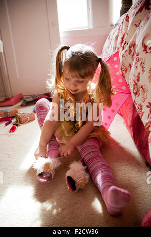 Jeune Fille en rose joue siège au sol avec une lumière vive derrière elle, essayant sur ses chaussures, jouer Dress-up dans sa chambre à coucher Banque D'Images