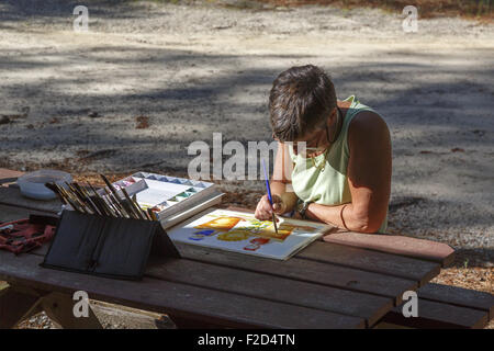 Artiste féminin assis à table à l'extérieur dans la lumière du soleil peinture partielle Banque D'Images