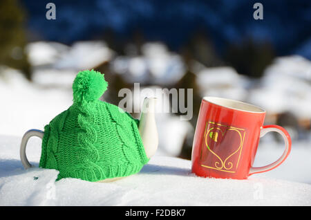 Pot de thé dans la tasse rouge et Chapeau tricoté avec un cœur dans la neige Banque D'Images