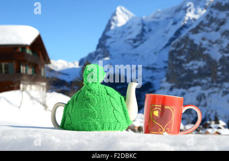 Pot de thé dans la tasse rouge et Chapeau tricoté avec un cœur dans la neige Banque D'Images