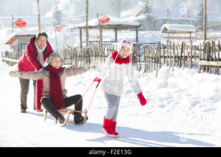 Famille heureuse de jouer avec traîneau dans la neige Banque D'Images