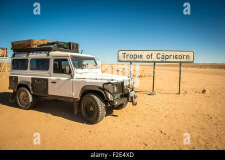 Land Rover Defender 110 stationnés dans le désert à côté d'un signe pour le Tropique du Capricorne en Namibie, Afrique Banque D'Images