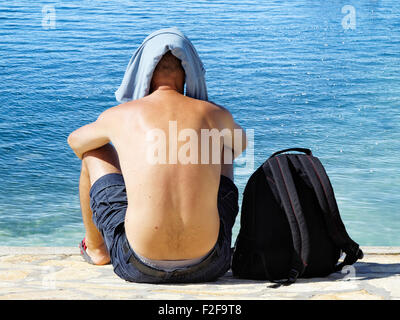 Jeune homme assis sur le littoral avec des t-shirt sur sa tête Banque D'Images