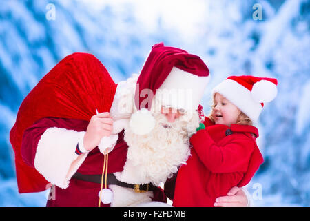 Le Père Noël et les enfants de l'ouverture présente dans la forêt enneigée. Les enfants et le père à Santa costume et beard ouvrir les cadeaux de Noël Banque D'Images