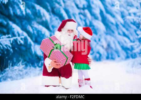 Le Père Noël et les enfants de l'ouverture présente dans la forêt enneigée. Les enfants et le père à Santa costume et beard ouvrir les cadeaux de Noël Banque D'Images