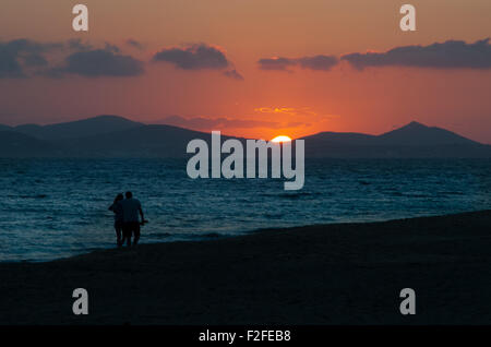 Couple en train de marcher le long de plage au coucher du soleil Banque D'Images