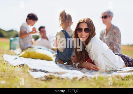 Portrait smiling woman laying on blanket in champ ensoleillé avec la famille Banque D'Images