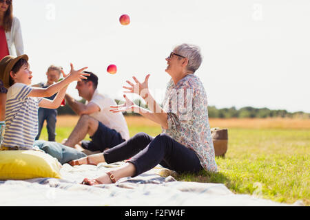 Grand-mère et petit-fils juggling pommes sur couverture de pique-nique dans le champ ensoleillé Banque D'Images