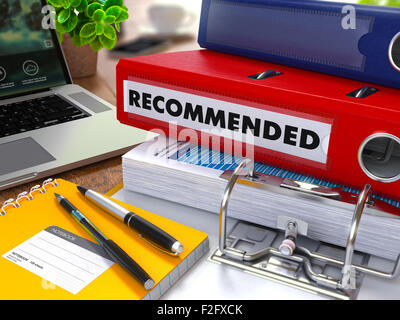 Classeur rouge avec l'Inscription recommandée sur la table de travail de fond avec les fournitures de bureau, ordinateur portable, des rapports. Tonique illustr Banque D'Images