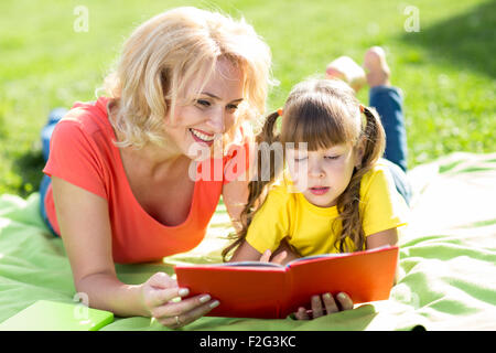 Mère et fille lire un livre dans le parc. Banque D'Images