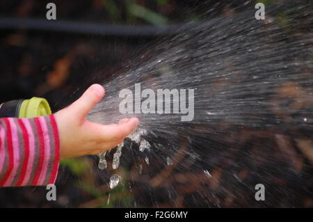 Un gros plan d'une petite fille jouant avec l'eau qui sort d'un tuyau Banque D'Images