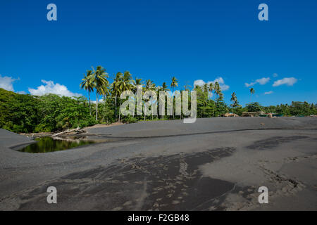 Cabanes de pêcheurs côtiers dans la région de Sulawesi du Nord sur une plage de sable noir avec lush tropical dans le contexte au cours d'une journée ensoleillée avec blue Banque D'Images