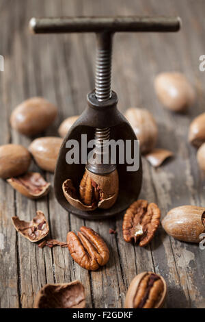 Pecan étant fissuré dans une antique Casse-noisette, entouré de pecan sur le bois brut Banque D'Images