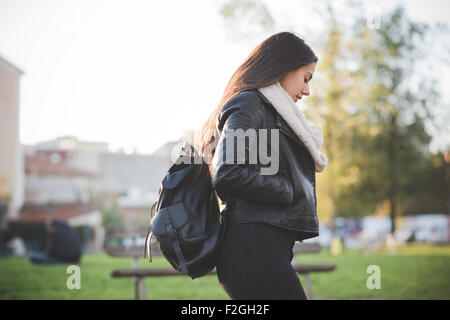 Profil de la demi-longueur d'une belle jeune femme cheveux longs en flânant dans un parc de la ville au coucher de rétro-éclairage Banque D'Images