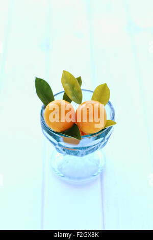 Entièrement mûres calamondin, Kumquat, Citrofortunella microcarpa dans un bol en verre sur planche de bois Banque D'Images