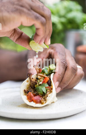 Un homme est squeezing lime sur une poitrine de boeuf mijotés chili taco en le maintenant avec son autre main. Banque D'Images