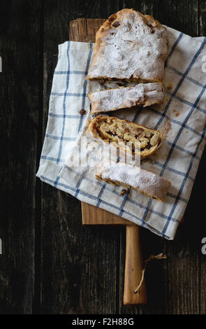 Maison de boulangerie frais tranchés strudel aux pommes sur une planche à découper sur l'ancien fond de bois. Style rustique foncé. La lumière naturelle du jour. Haut Banque D'Images