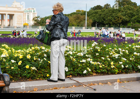 Moscou, Russie. Samedi, 19 Septembre, 2015. Week-end chaud. C'est confortable d'être à l'extérieur. Un inconnu, méconnaissable senior woman prend une photo de roses blanches et jaunes sur un parterre de Gorky Park. Son bâton de marche se trouve sur le terrain. Entrée principale du parc peut être vu dans l'arrière-plan (à gauche). Crédit : Alex's Pictures/Alamy Live News Banque D'Images