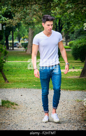 Beau jeune homme en t-shirt blanc et un jean en plein air du parc de la ville, marcher vers la caméra, de graves Banque D'Images