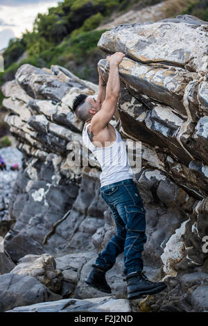 Trois quart d'un joli coup de jeune homme athlétique escalade un rocher à la rivière ou à la mer ou l'Océan Banque D'Images