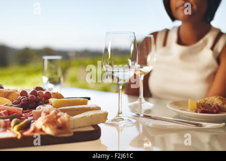 Set de table dans la cave avec deux verres de vin, fromage et raisin. Femme assise à l'arrière au restaurant cave table. Banque D'Images