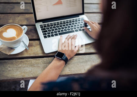 Femme de taper au clavier d'un ordinateur portable avec une tasse de café sur la table en bois. Femme portant une smartwatch au café. Banque D'Images