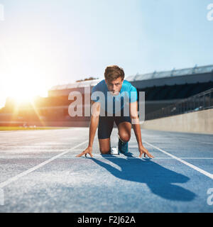 Mettre en place et l'homme confiant en position de départ prêt pour la course. À propos de l'athlète masculin pour démarrer un sprint looking at camera with bright Banque D'Images