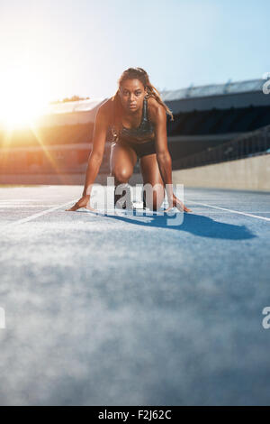 Shot verticale de jeunes femmes sprinter en tenant prêt à démarrer face à la caméra. Femme athlète en blocs de départ avec Banque D'Images