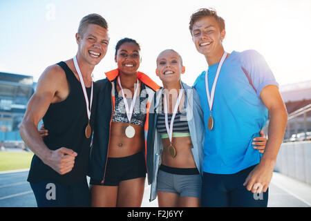 Heureux de célébrer la victoire des athlètes multiraciale debout ensemble sur des courses. Groupe de runner avec des médailles gagner une compe Banque D'Images