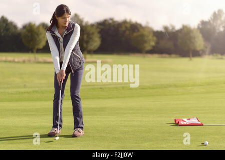 Golfeuse attrayant pour mettre le trou sur le green à l'aide d'un putter et regarder la balle de golf vers la tasse de rouleau Banque D'Images