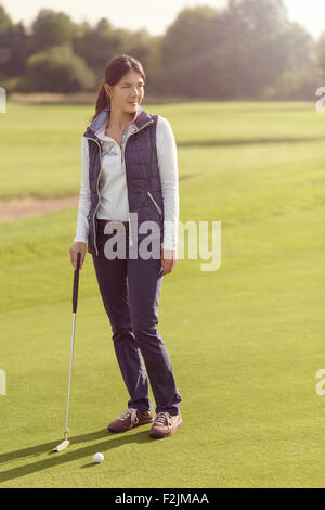 Golfeuse attrayants debout sur le vert avec son putter, détournant avec concentration à la prochaine grève Banque D'Images