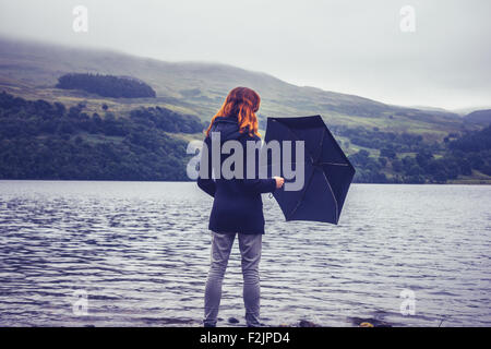 Jeune femme avec parapluie par le lac en automne Banque D'Images