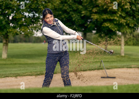 Golfeur femme jouant d'un bunker de sable sur un terrain de golf avec le sable battant du club qu'elle entraîne son shot Banque D'Images