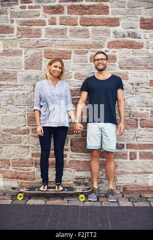 Young couple holding hand leaning against wall Banque D'Images