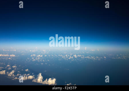 Vue aérienne Nuages blancs Ciel bleu Horizon Jour Depuis la fenêtre de l'avion | MEXIQUE — Une vue à haute altitude depuis la fenêtre d'un avion montre des nuages cumulus dispersés sur un horizon courbé, le ciel passant d'un bleu pâle près de la surface à un noir presque total au bord de la stratosphère. De telles vues sont courantes lors de la descente vers Mexico, dont l'aéroport, situé à haute altitude, se trouve à environ 7 300 pieds (2 225 m). Le dégradé illustre comment la densité atmosphérique diminue avec l'altitude,散射 moins de lumière et assombrit le ciel au-dessus. Banque D'Images