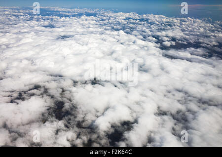 Vue aérienne en altitude en lumière du jour de nuages blancs vus d'en haut avec un ciel bleu | MEXIQUE — Une couche dense de nuages cumulus blancs s'étend sous un ciel bleu clair dans cette vue en altitude depuis une fenêtre d'avion, avec des zones de terrain sombre visibles à travers les interstices de la couverture nuageuse. La formation est typique de l'activité convective diurne sur le Mexique central, où l'air chaud ascendant produit des champs de nuages cumulus gonflés à des altitudes généralement inférieures à 6 500 pieds (2 000 m). La photographie a été prise depuis un avion commercial pendant un vol sur le pays. Banque D'Images