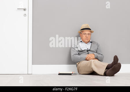 Représentant principal de dormir assis sur le sol et appuyée contre un mur à côté d'une porte blanche avec quelques livres à côté de lui Banque D'Images