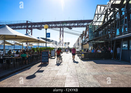 La fin de l'après-midi boutiques et restaurants brillent sous le pont 25 de Abril. Banque D'Images
