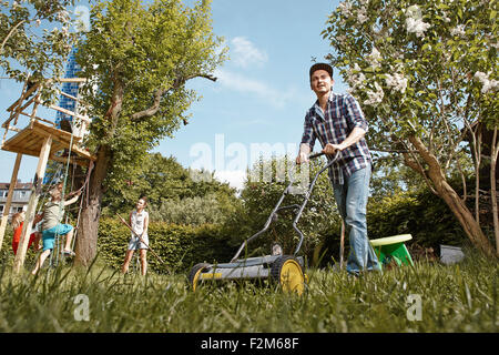 Man mowing lawn dans le jardin avec la famille en arrière-plan Banque D'Images