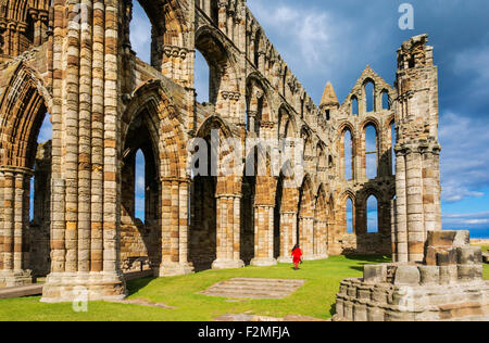 Les ruines de l'abbaye de Whitby avec un ciel orageux et une seule figure en manteau rouge Whitby North Yorkshire Angleterre Grande-Bretagne Royaume-Uni GB Europe Banque D'Images