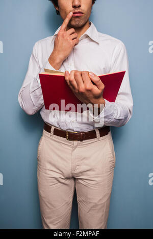 Jeune homme debout par un mur bleu reading book Banque D'Images