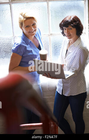 Deux femmes d'affaires avec ordinateur portable ayant Réunion informelle In Office Banque D'Images