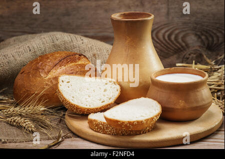 Pain et produits de boulangerie, et le lait dans un pot en argile et le bol, les tiges de blé, de la toile de jute sur le vieux fond de bois Banque D'Images