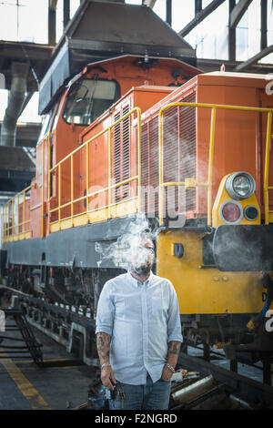 Caucasian man blowing smoke in train yard Banque D'Images