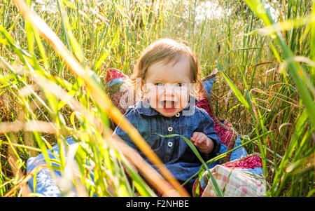 Caucasian baby girl sitting in tall grass Banque D'Images