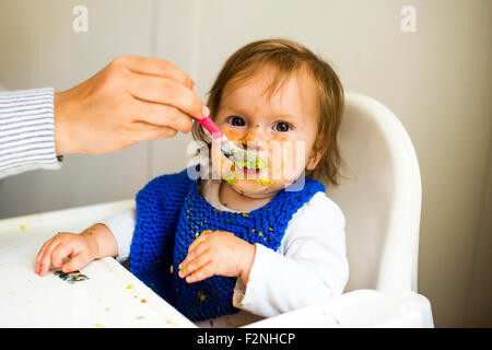 Mère nourrir bébé fille dans une chaise haute Banque D'Images
