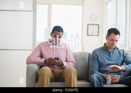 Les hommes avec des téléphones de l'attente sur canapé Banque D'Images