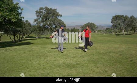 Caucasian couple transportant des sacs de golf on course Banque D'Images